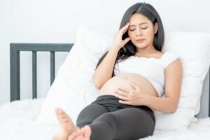 Kopfschmerzen in der Schwangerschaft: Schwangere sitzt auf dem Bett