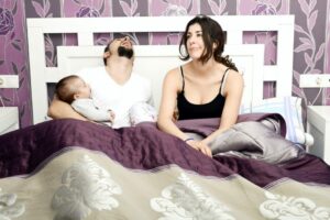 Paar im Bett mit Baby, Mann schläft: Junge Eltern haben keine Lust auf Sex, nach der Geburt des Babys