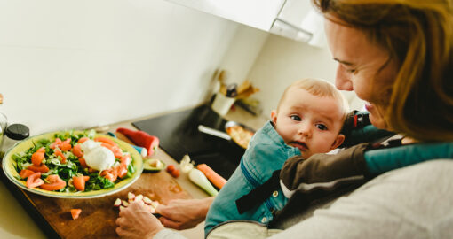 Mutter mit Babytrage bereitet frisches Essen zu