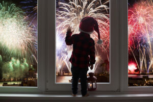 Kleinkind steht am Fenster und beobachtet das Feuerwerk