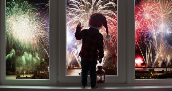 Kleinkind steht am Fenster und beobachtet das Feuerwerk