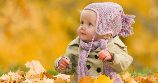 Baby sitzt im Herbst in einem Blätterhaufen
