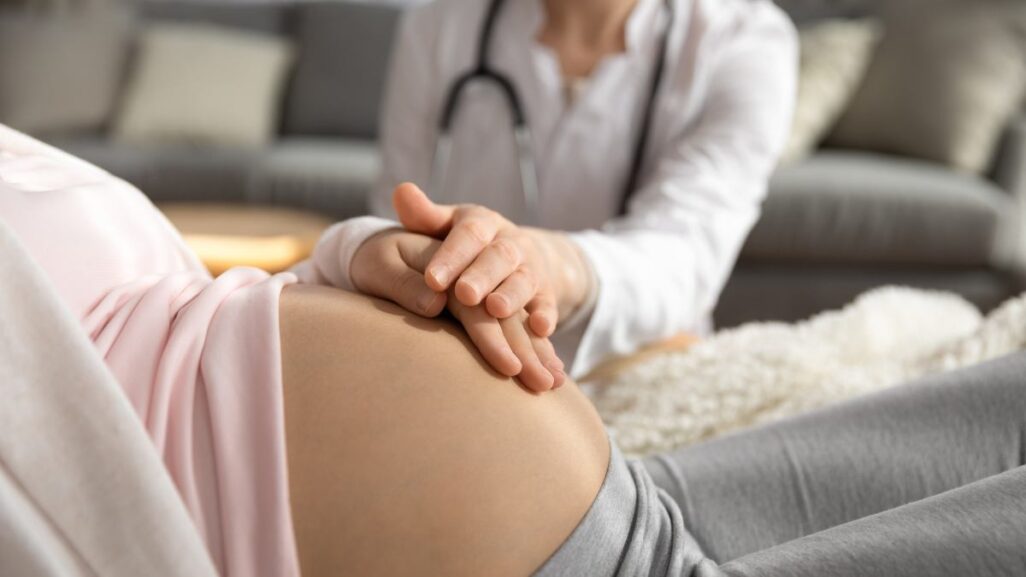 Babybauch mit Hand der Mutter und Ärztin drauf