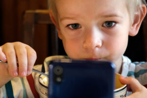Kleiner Junge schaut beim Essen einen Film auf dem Handy