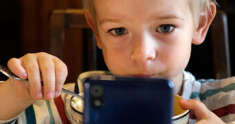 Kleiner Junge schaut beim Essen einen Film auf dem Handy