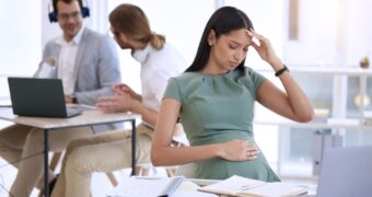Schwangere Angestellte im Büro, fasst sich an Bauch und Kopf