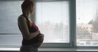 Schwangere Frau hat Angst vor einem Kaiserschnitt und blickt sorgenvoll aus dem Fenster.
