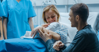 Frau hält nach der natürlichen Geburt nach Kaiserschnitt ihr Baby im Arm.