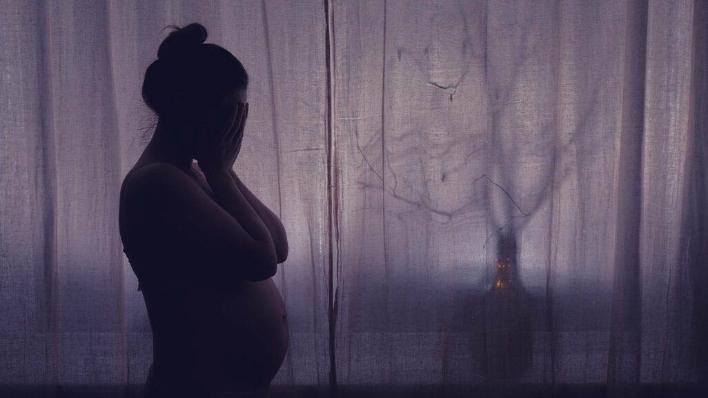 Schwangere mit Tokophobie steht in dunklem Zimmer und kann nicht schlafen